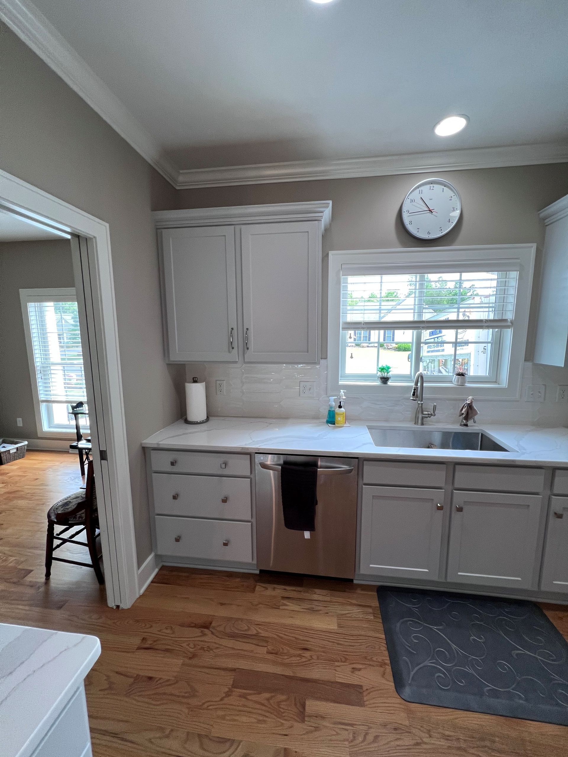 Kitchen with white cabinets, window over sink, clock, and unfinished lower cabinets.