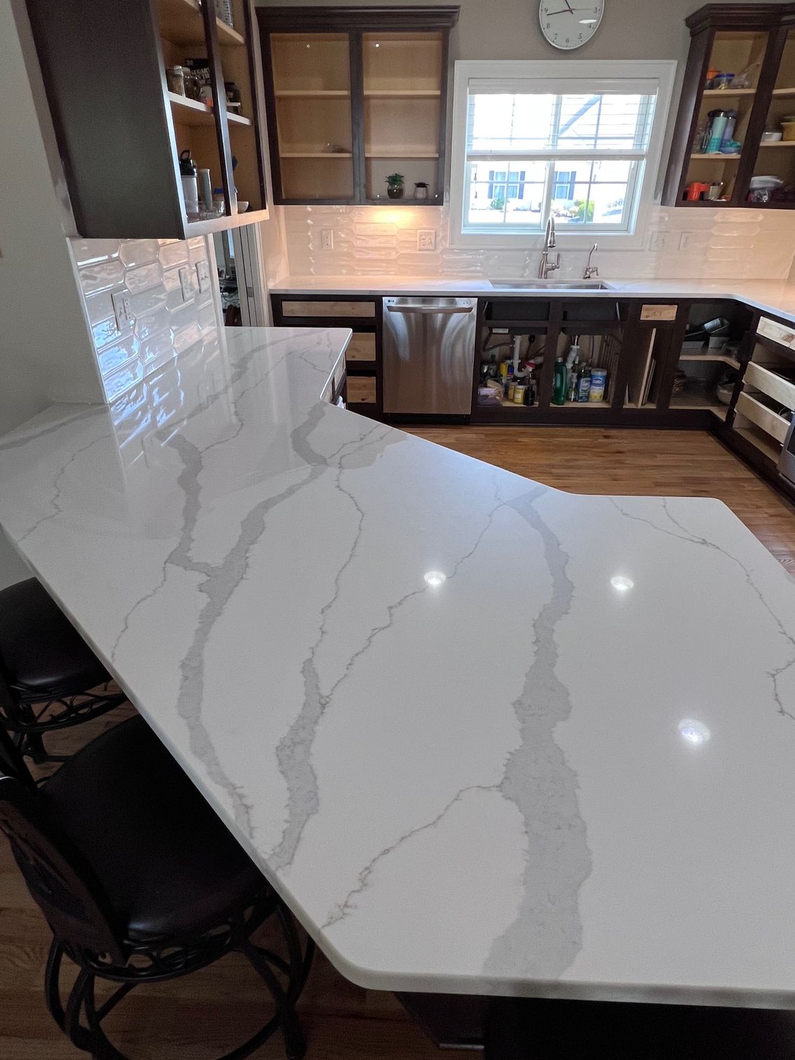 Bright kitchen with large white quartz island, wood cabinets, tile backsplash, and window over the sink.