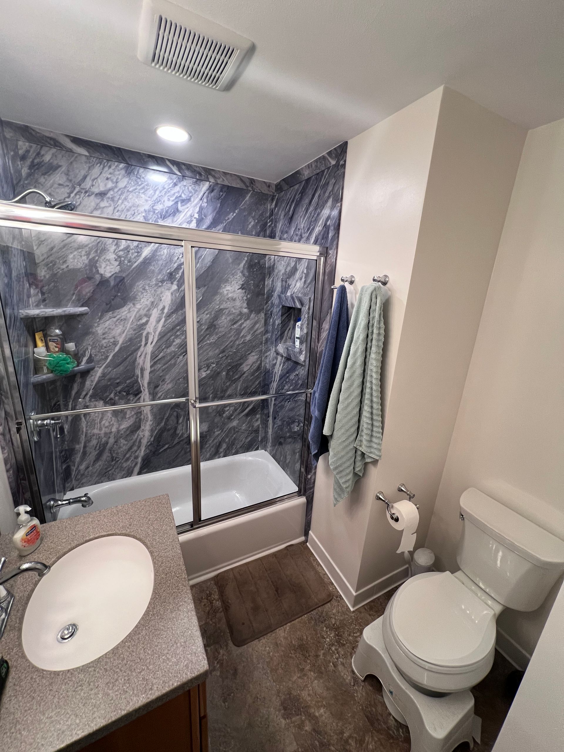 Small bathroom with shower, toilet, sink vanity, and towel rack; gray tile and marble-look shower walls