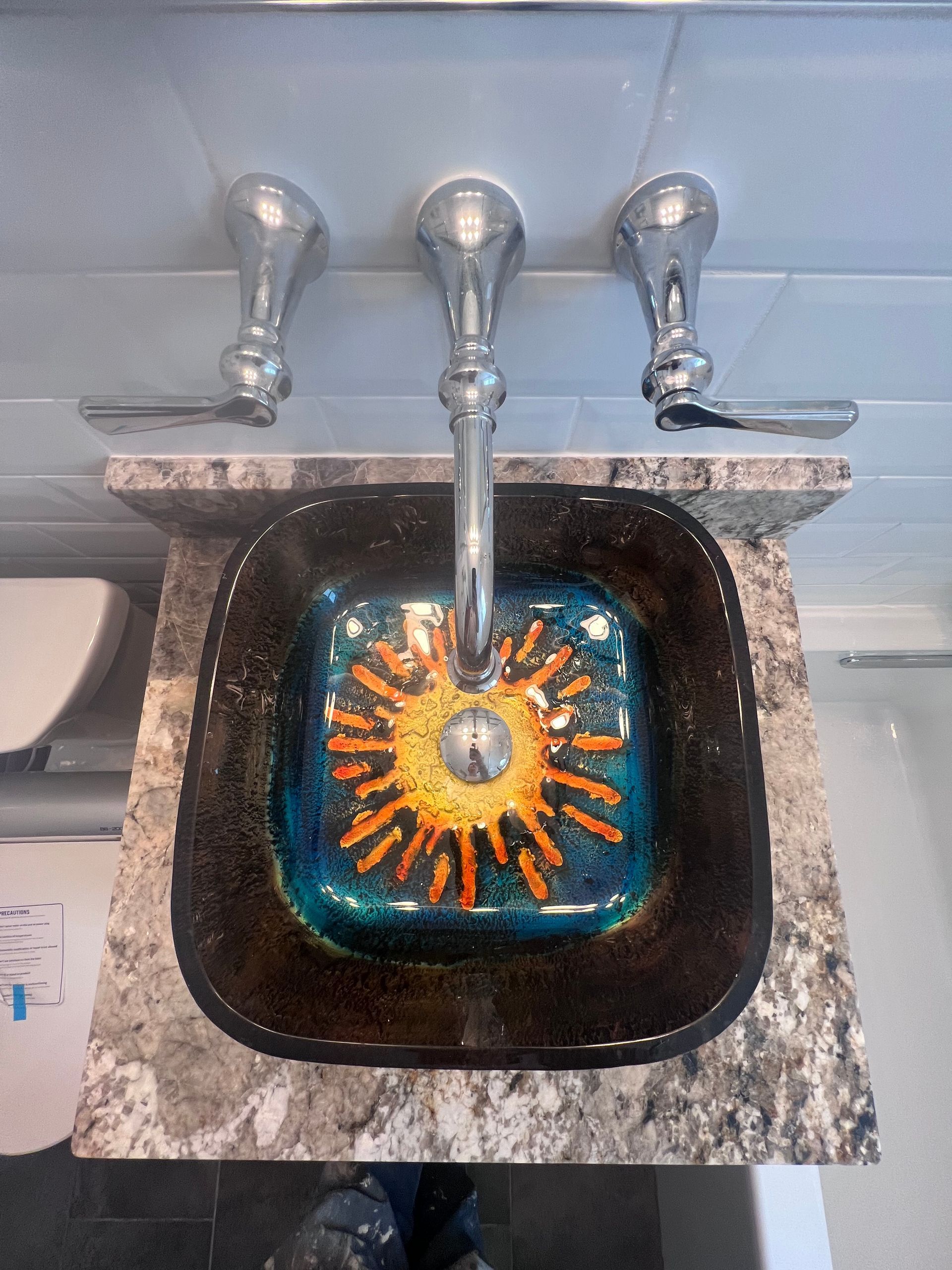 Bathroom sink with chrome faucet over a black basin and colorful sunburst design in the drain.