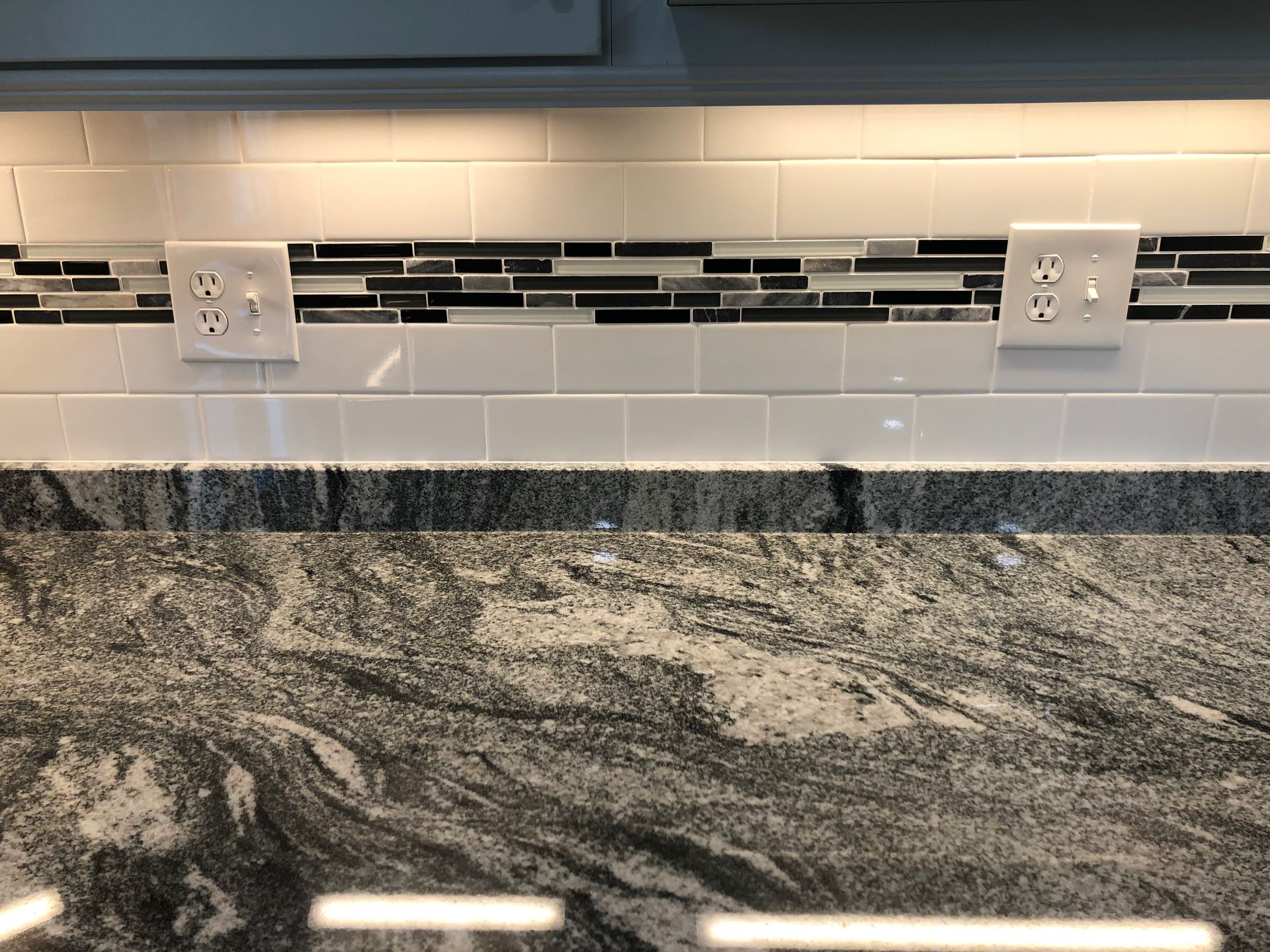 Kitchen backsplash with white subway tile, black mosaic accent strip, outlets, and granite countertop