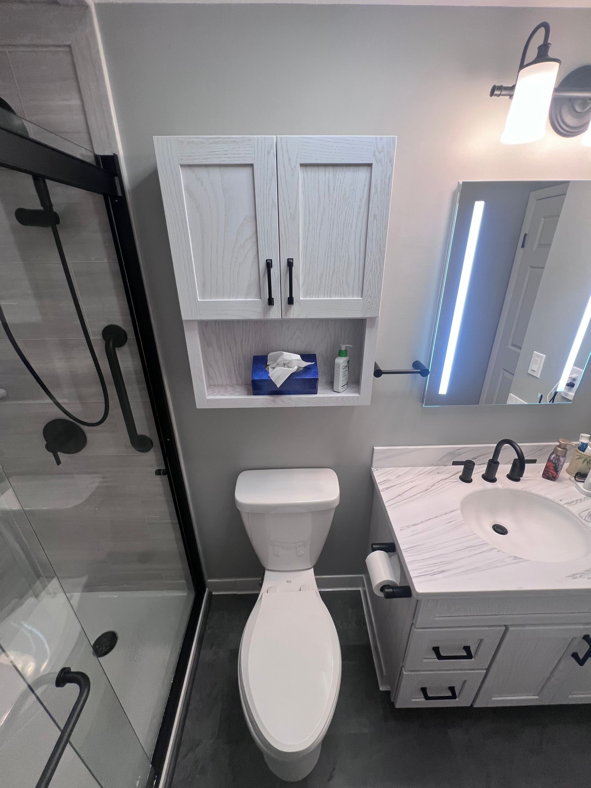 Small bathroom with walk-in shower, toilet, sink vanity, and wall cabinet in gray and white.