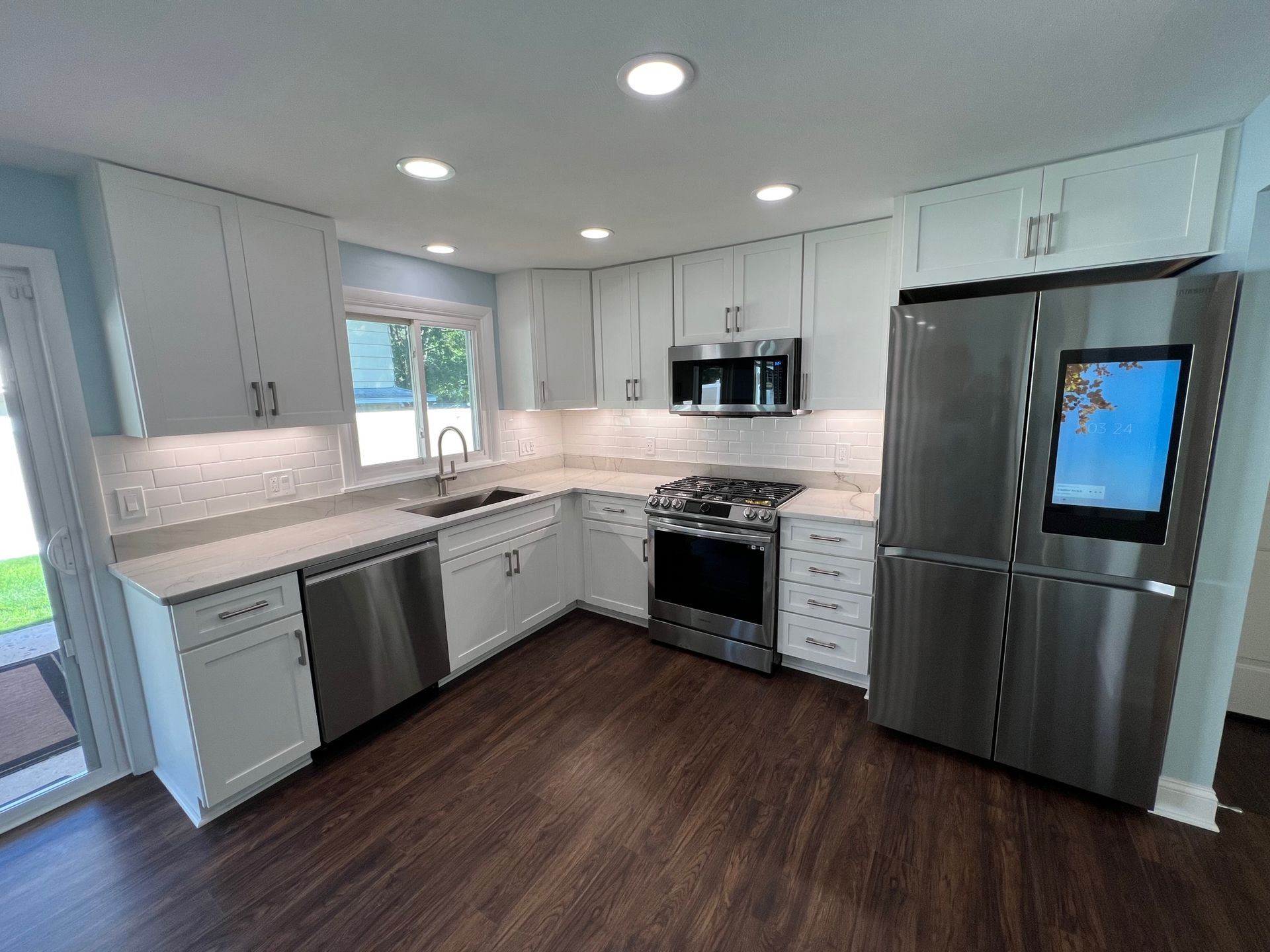 Modern white kitchen with dark wood floors, stainless appliances, and gray cabinets