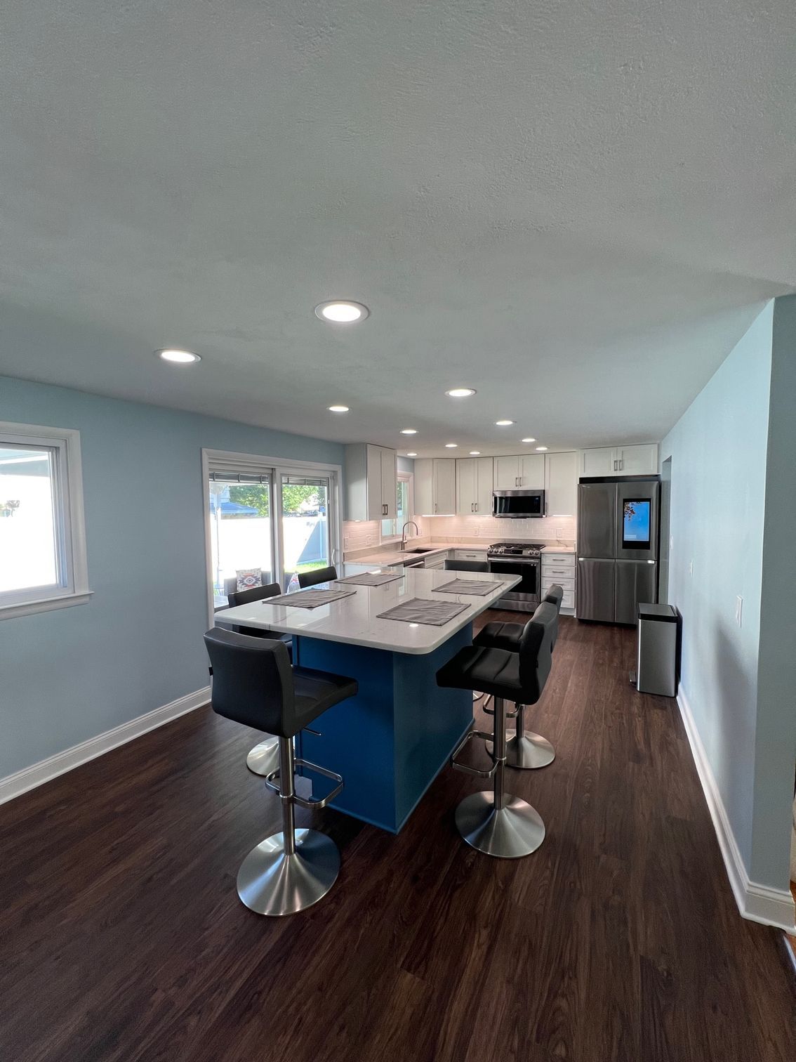 Modern kitchen with dark wood floors, blue island, barstools, and stainless steel appliances
