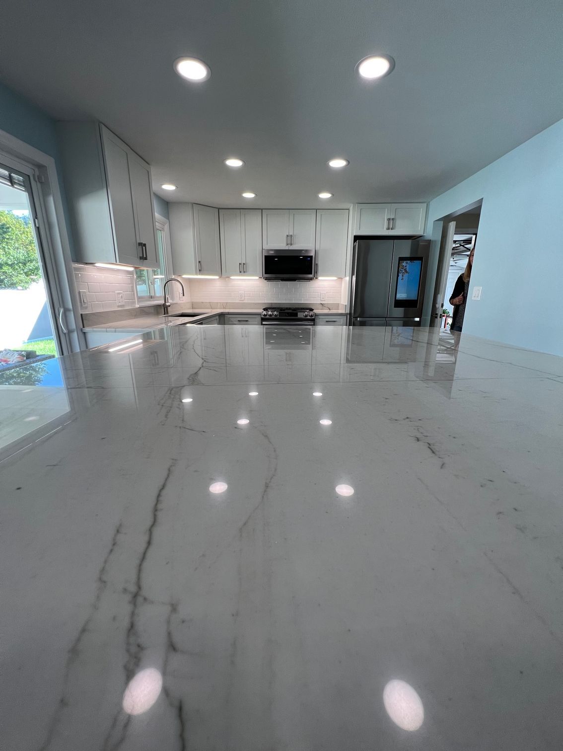 Bright modern kitchen with glossy marble floor, white cabinets, and recessed ceiling lights.