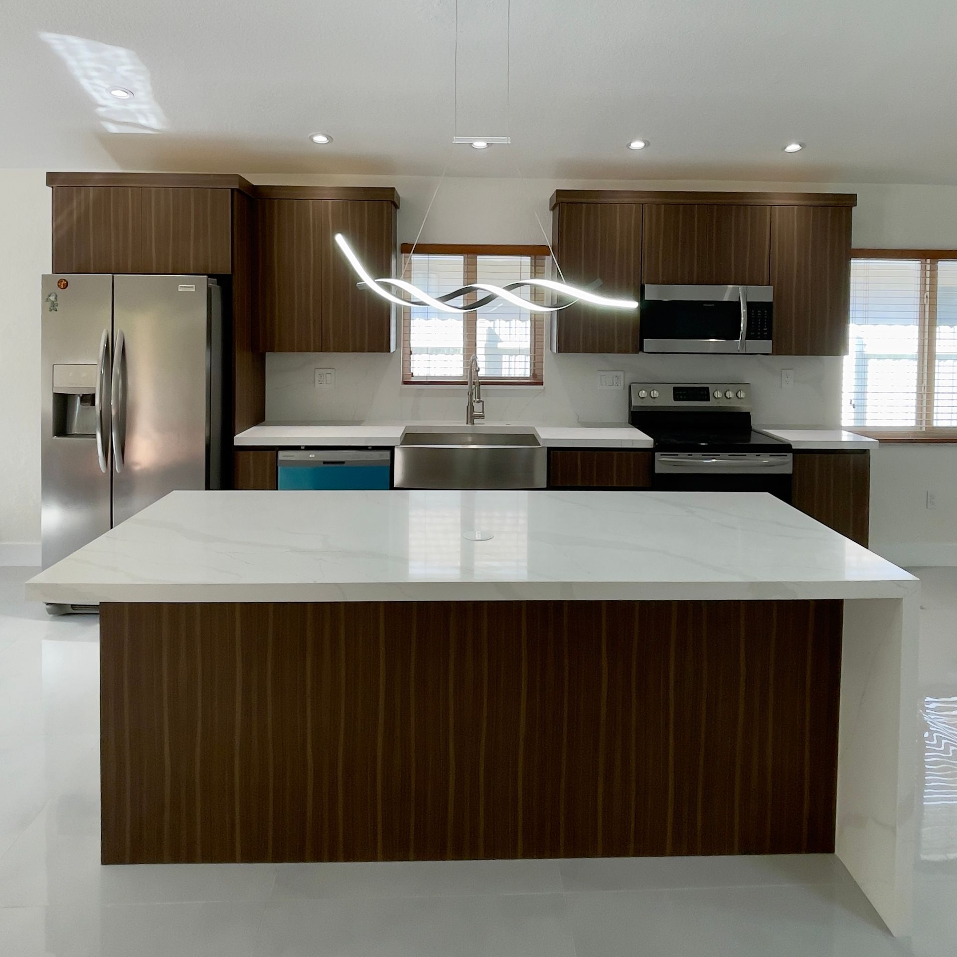 Modern kitchen with dark wood cabinets, white countertops, and a large island.