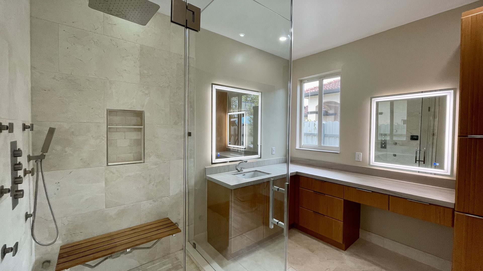 Modern bathroom with a glass shower, wooden vanity, and illuminated mirrors.