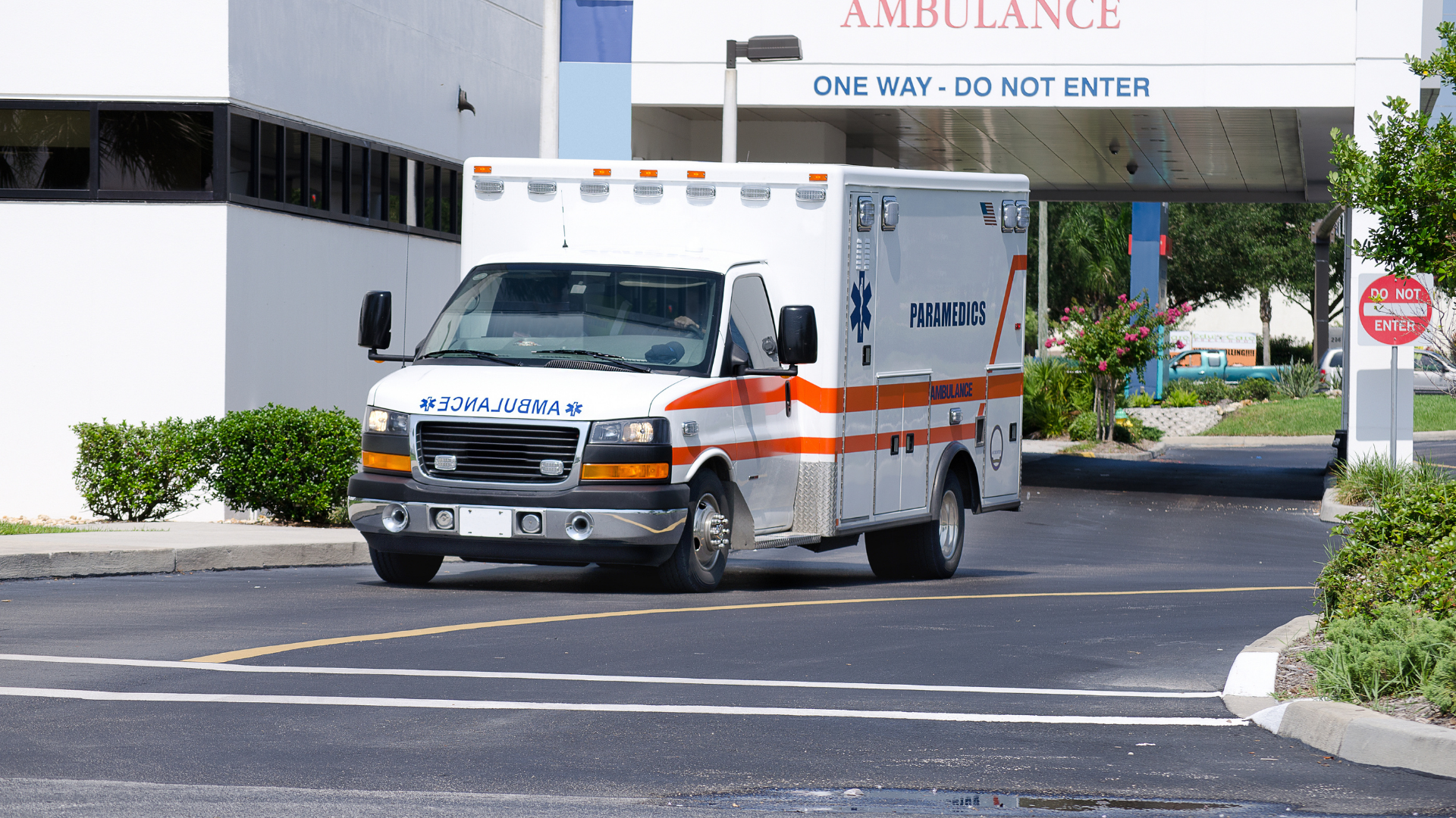 A white ambulance with orange stripes drives toward a building with a 