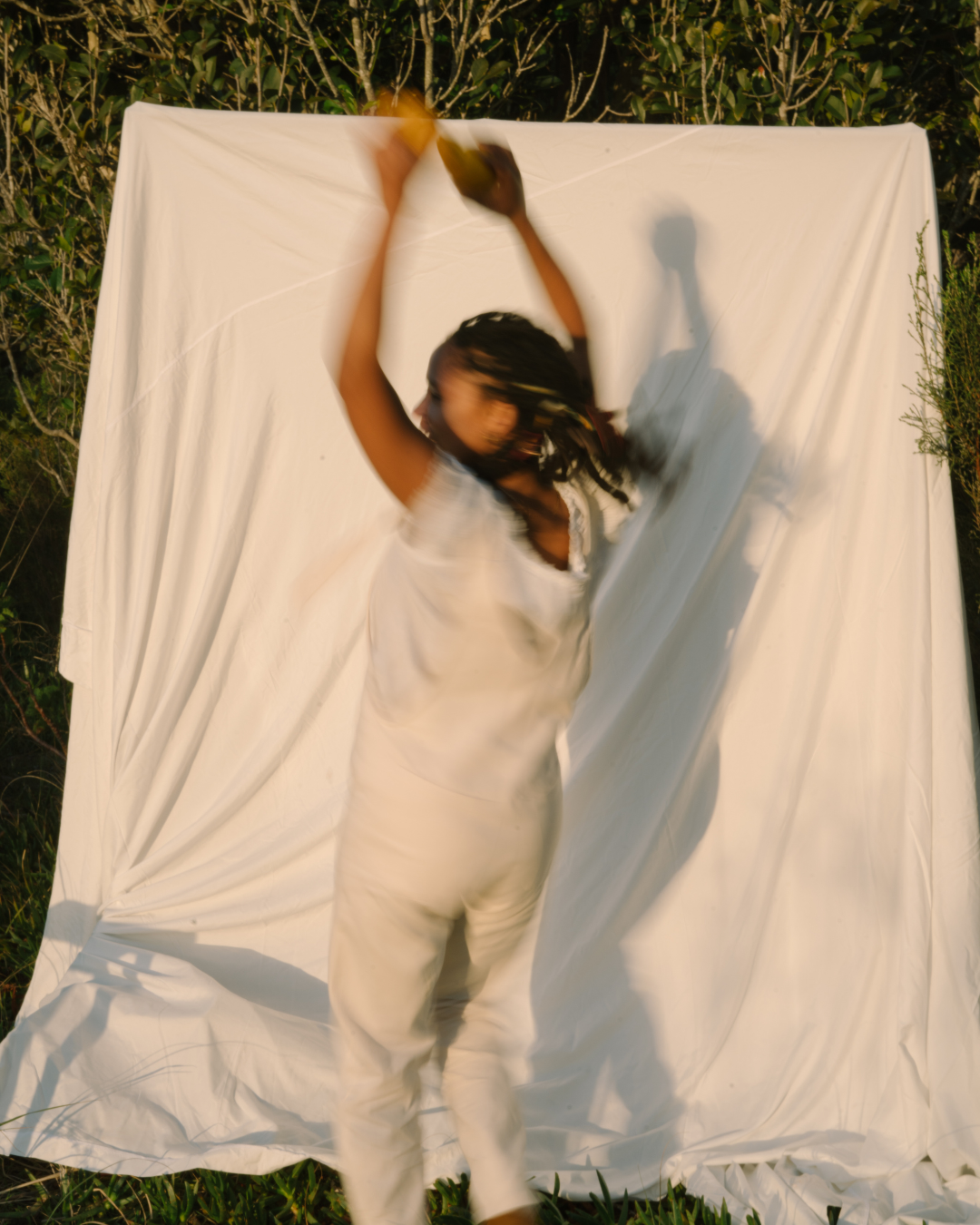 Person in white clothes dancing before a white sheet backdrop outdoors.