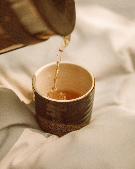 Hot tea being poured into a small cup on a soft blanket.