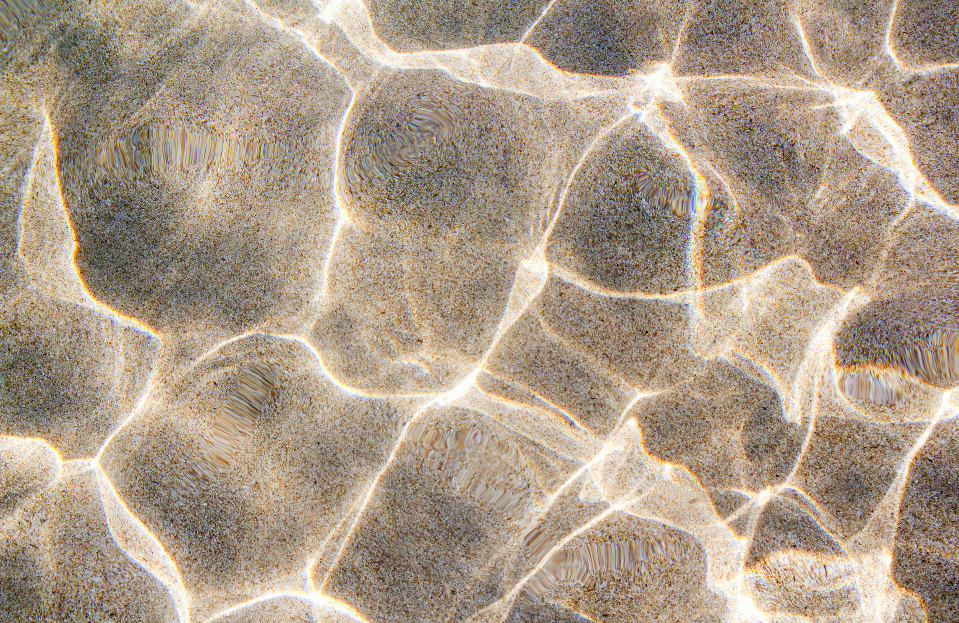 Sunlit ripples on clear water over a sandy bottom, creating a bright abstract pattern