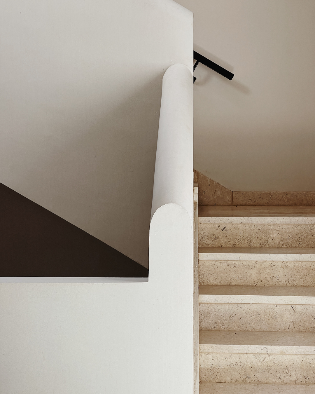 Indoor staircase with beige steps, white wall, and a black handrail at the landing.
