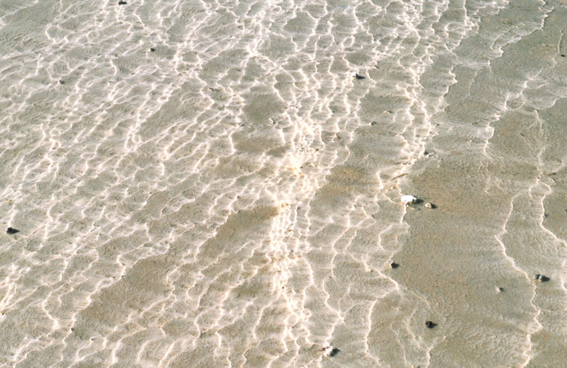 Rippling shallow seawater over wet sand with small dark pebbles at right