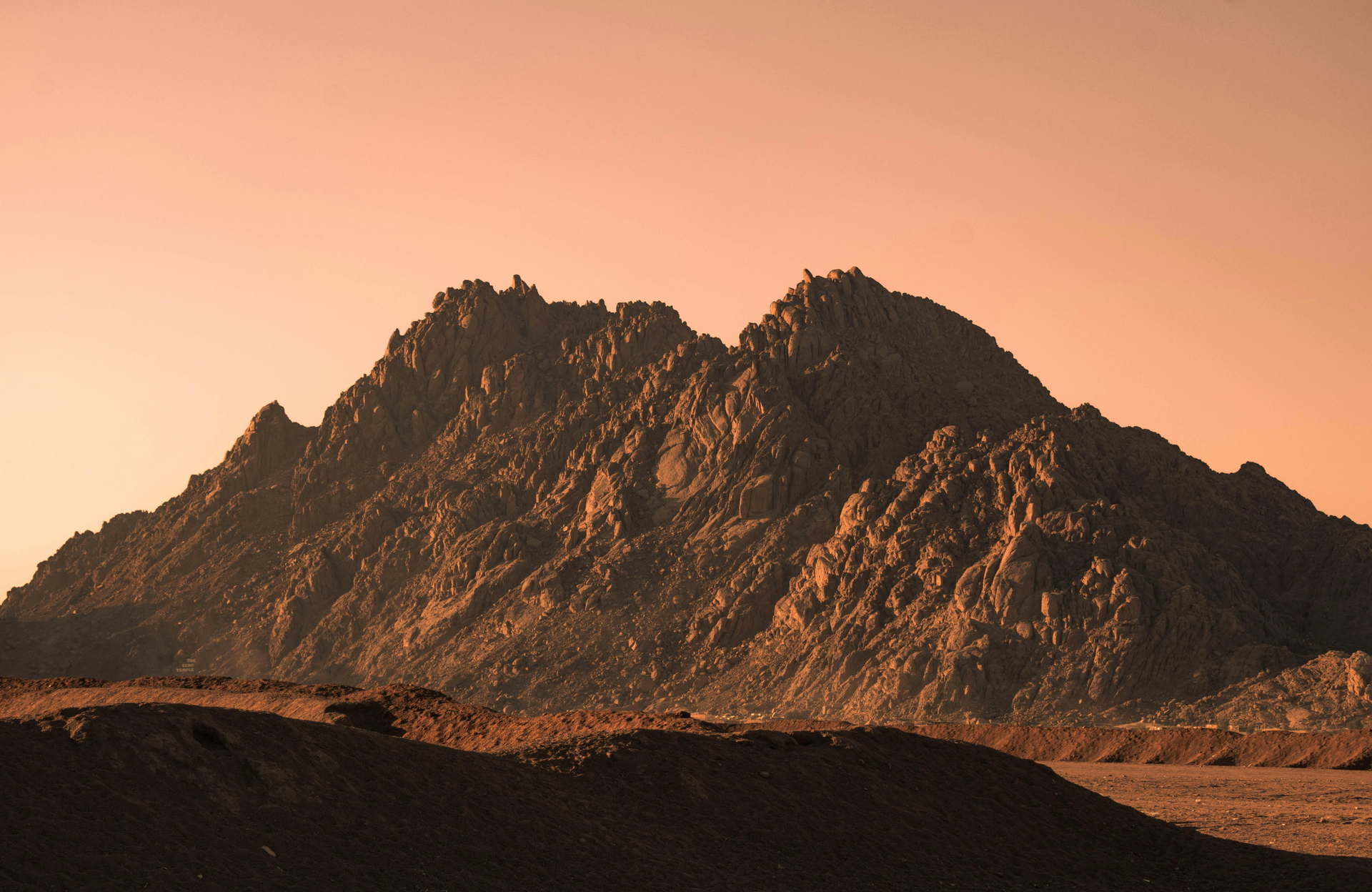 Rocky mountain silhouette at sunset under a warm pink-orange sky