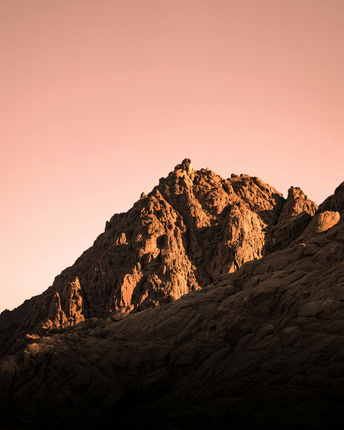 Sunlit rocky mountain peak against a pink sunset sky