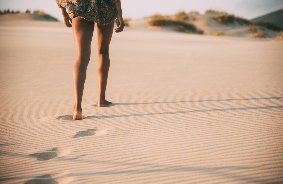 Bare legs walking barefoot across sunlit desert sand dunes