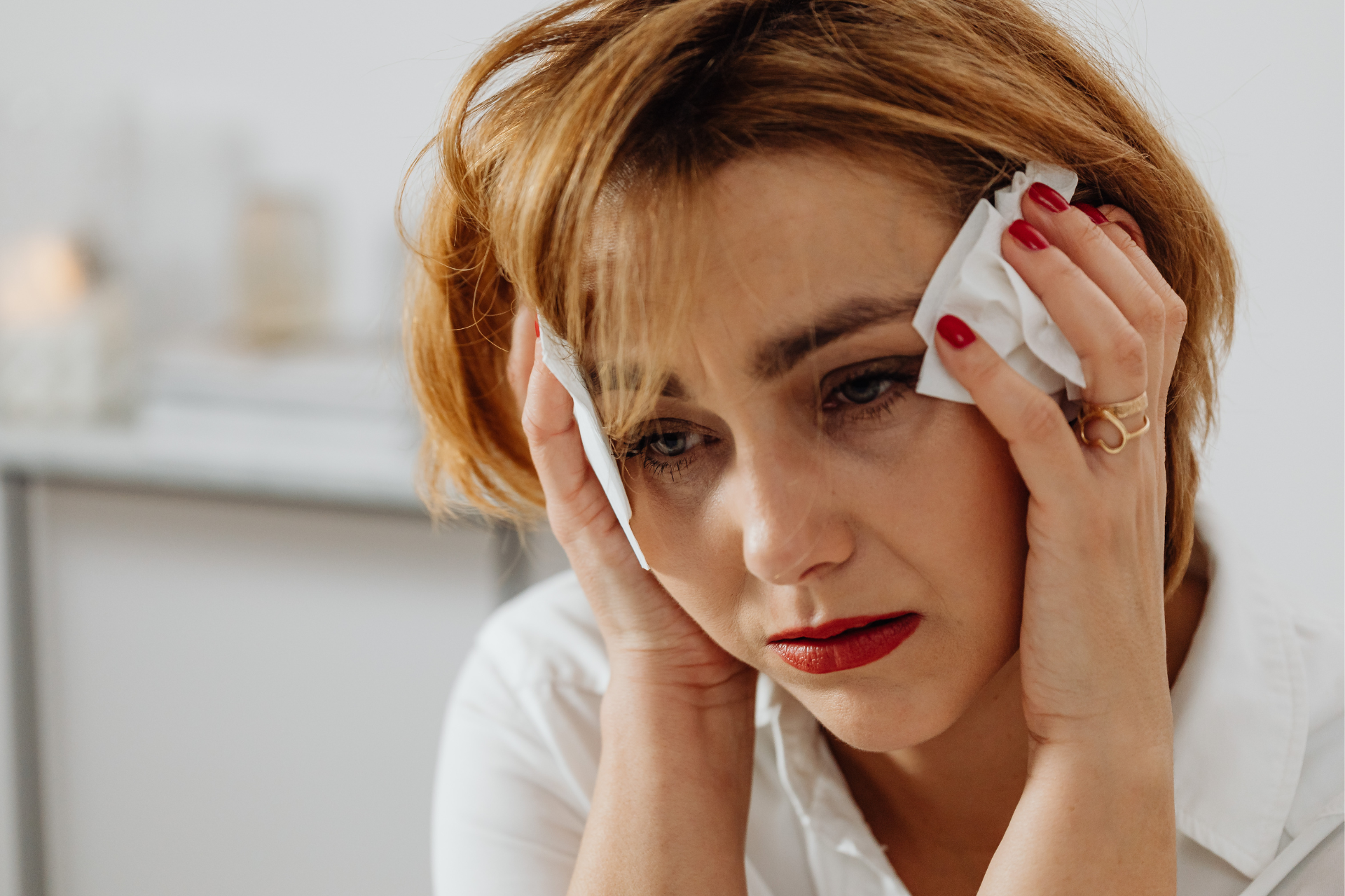 Person holding tissues to their face, looking distressed with a red nose indoors