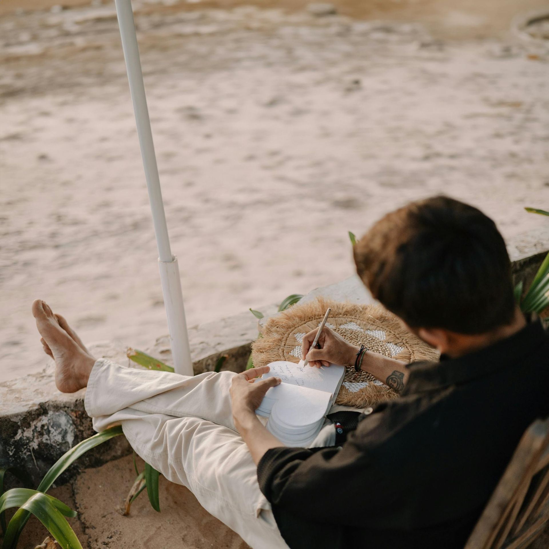 Person reclining on a lounge chair, writing in a notebook by the water