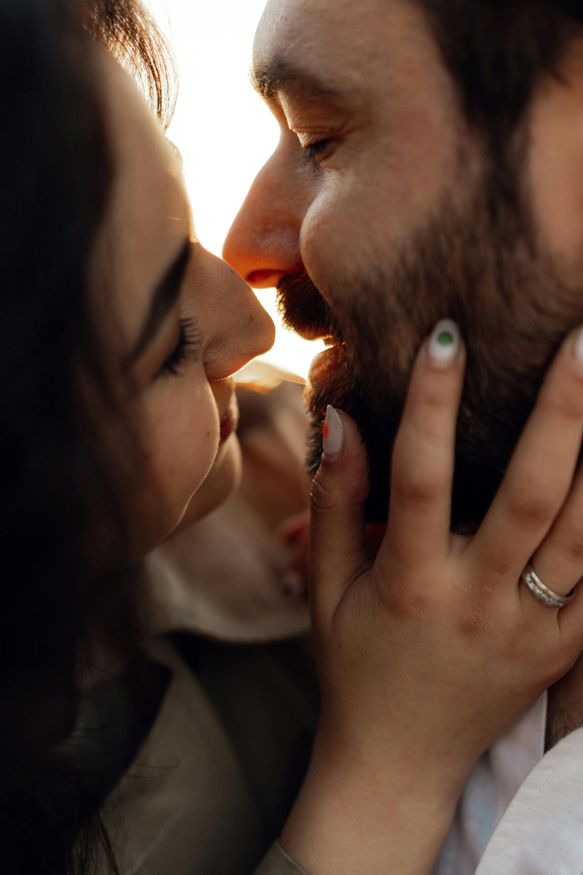 Close-up of two people kissing, with warm sunlight and a hand gently holding a face.