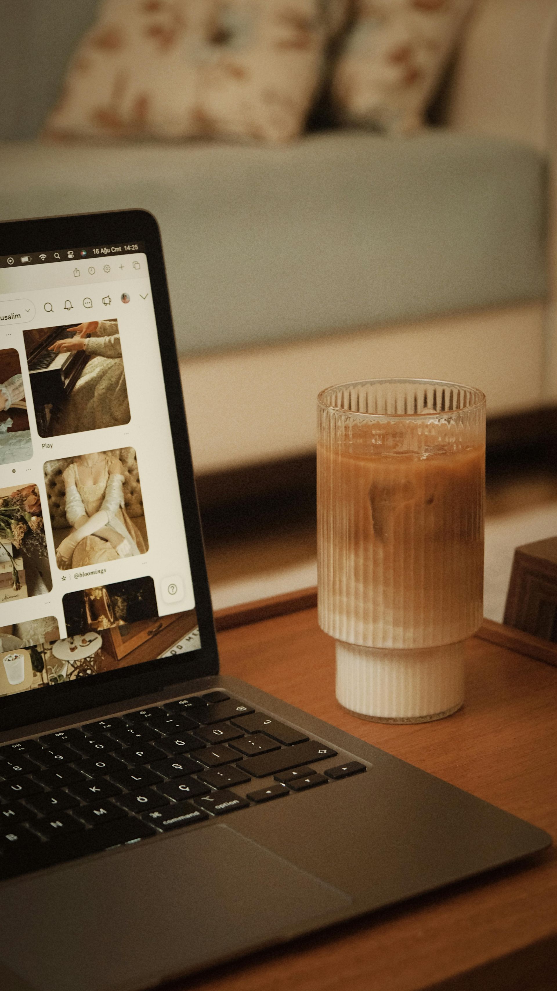 Laptop on a table with a drink in a glass beside it, in a warm, cozy room.