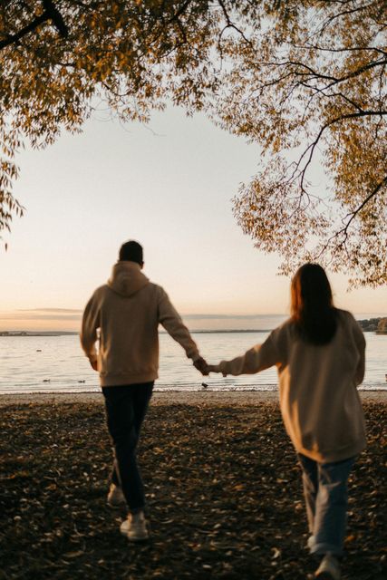 Two people holding hands while walking on a beach at sunset under overhanging tree branches