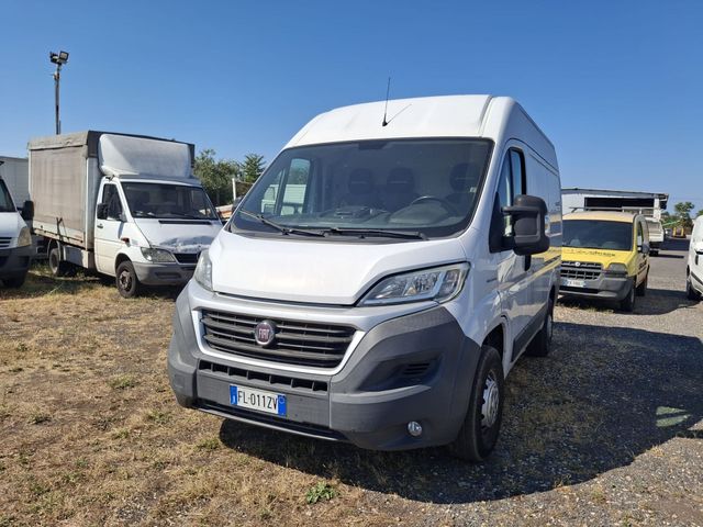 Un furgone bianco per il trasporto merci parcheggiato su un piazzale ghiaioso sotto un cielo azzurro, con altri veicoli commerciali sullo sfondo.