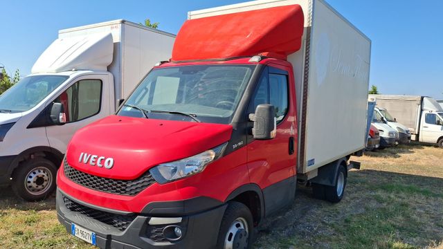 Un camioncino Iveco rosso è parcheggiato all'aperto in un piazzale, con dei furgoni bianchi per le consegne alle sue spalle.