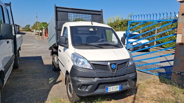 Furgone bianco parcheggiato vicino a un cancello blu in un parcheggio esterno soleggiato.