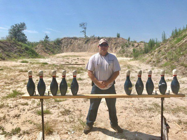 Man standing in front of ten bowling pins on a shooting range. Blue sky.