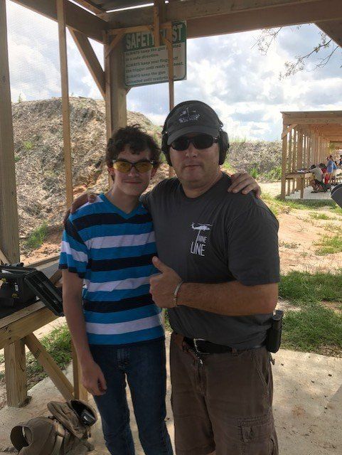 Two people posing at an outdoor shooting range. One man gives a thumbs up.