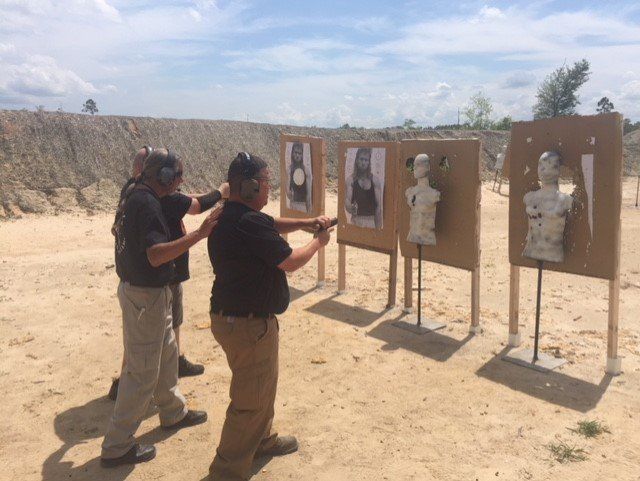 Two men practicing shooting at targets on an outdoor range, under a bright sky.