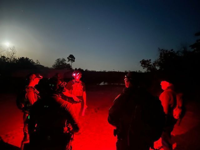 Group of people with red lights at night, possibly in a forest.