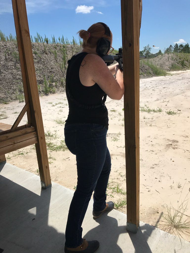 Woman with a rifle at an outdoor shooting range, wearing ear protection, aiming.