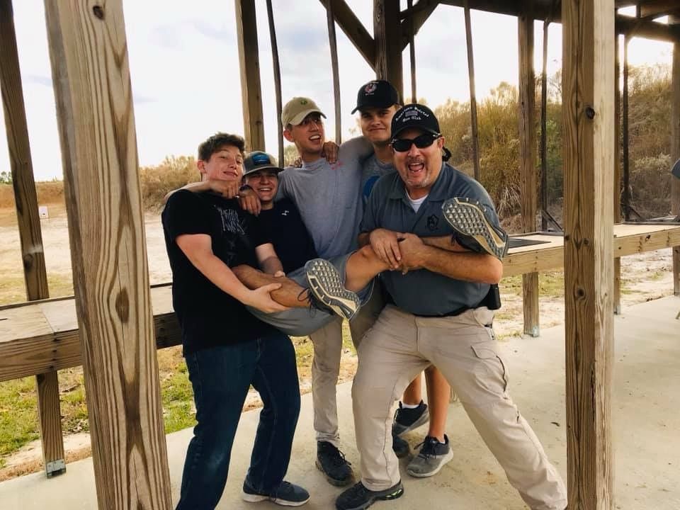 Five men smiling and playfully lifting another man at an outdoor shelter.
