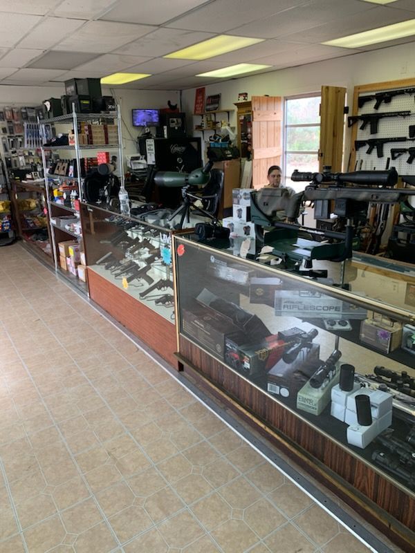 Inside a gun store: guns in display cases, a person behind the counter, various items for sale.