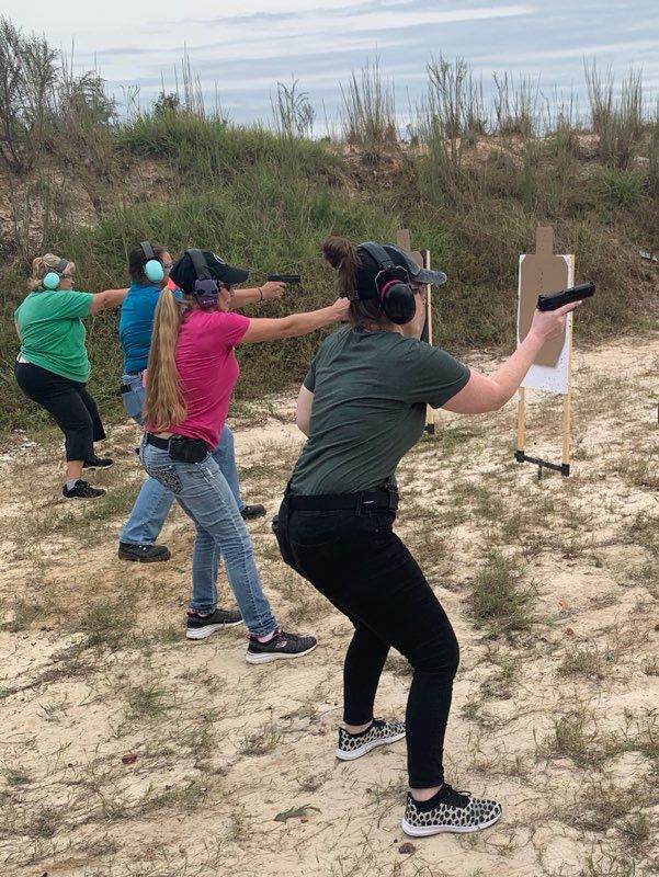 Four people with guns aiming at targets in a shooting range.