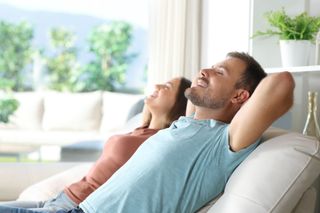 Two people relaxing on a sofa in a bright living room, leaning back with eyes closed. Two people relaxing on a sofa in a bright living room, leaning back with eyes closed.