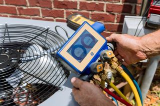 Technician handling HVAC gauges and hoses beside an outdoor AC unit and fan Technician handling HVAC gauges and hoses beside an outdoor AC unit and fan