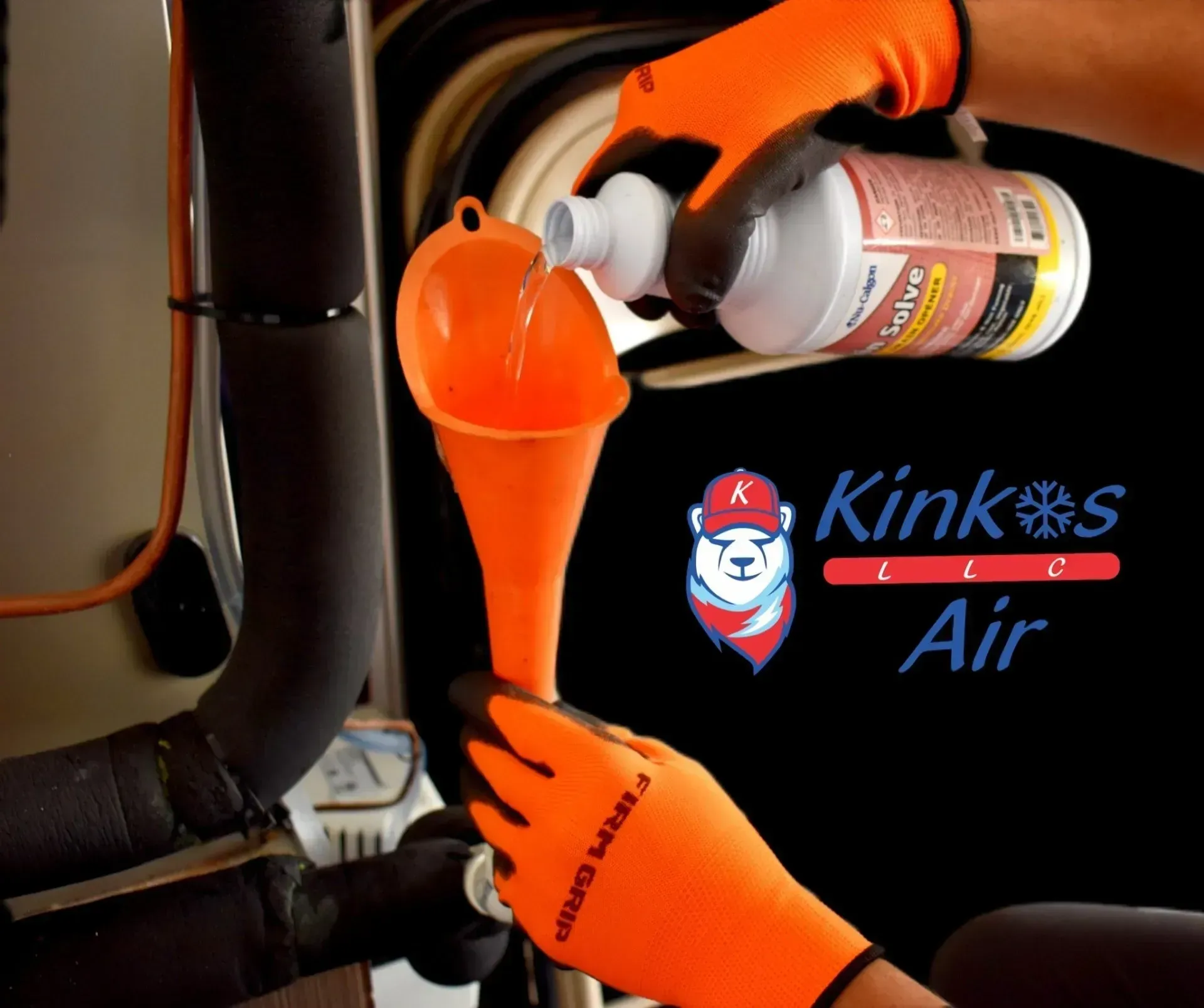 Orange-gloved hands pour liquid from a bottle into a funnel in a black Kink’s Air work shirt.