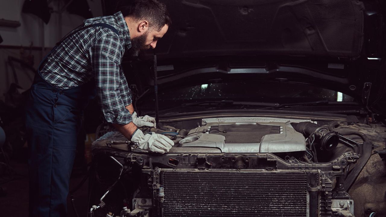Professional auto mechanic inspecting a car engine under the hood during routine vehicle repair and maintenance service.