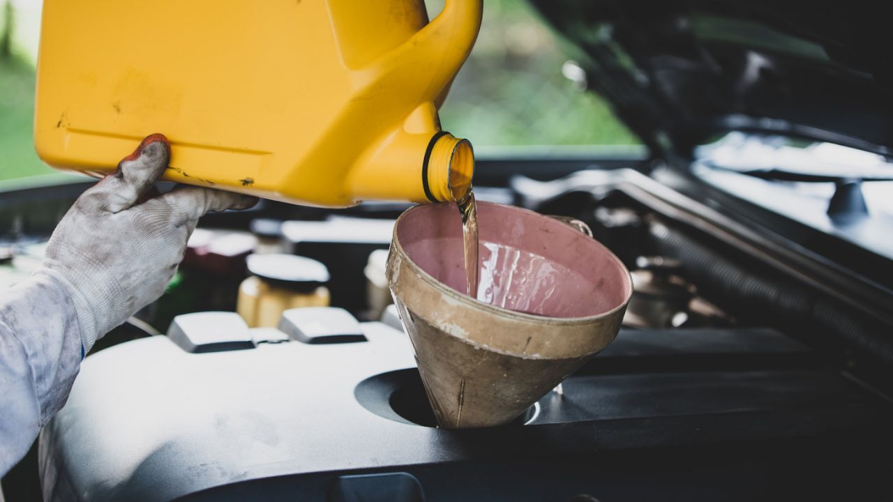 Pouring brake fluid into a car using a funnel.