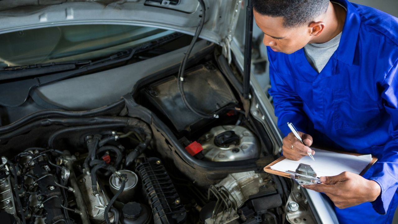 Vehicle technician filling out an inspection checklist next to an open car hood.  
