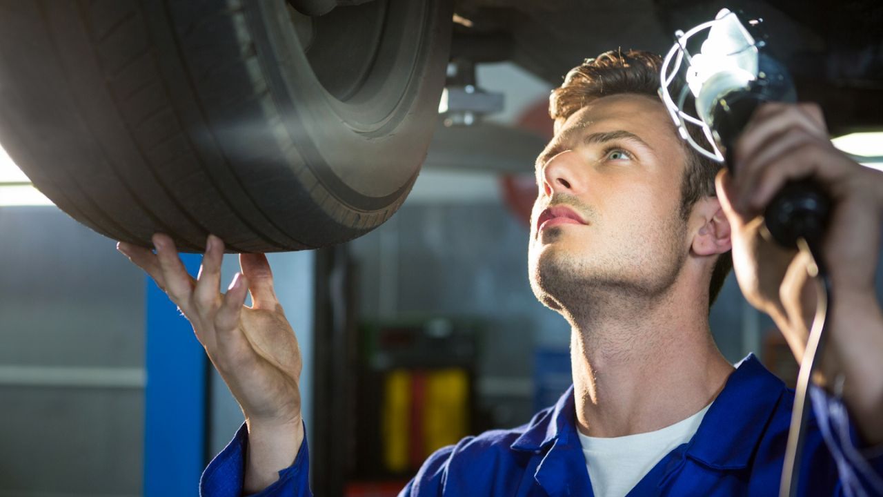 Mechanic inspecting car wheel and suspension using a work light