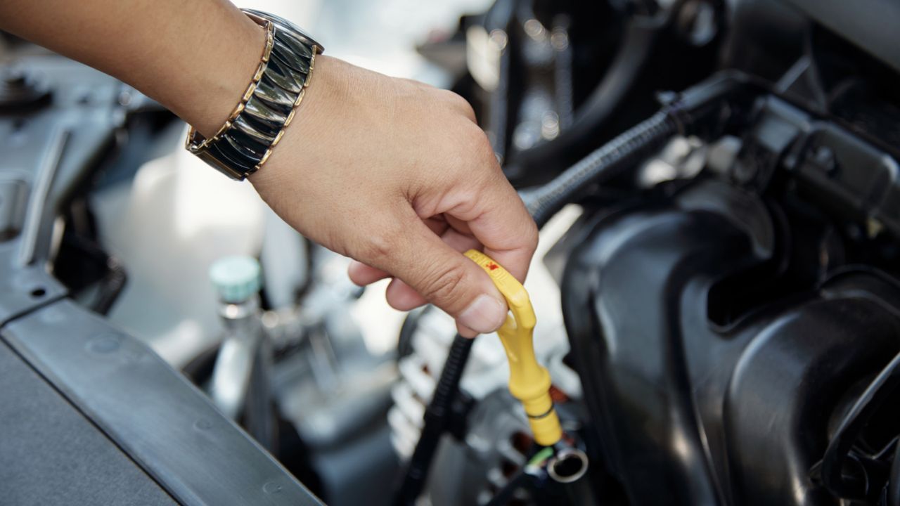 Hand pulling oil dipstick to check engine oil condition