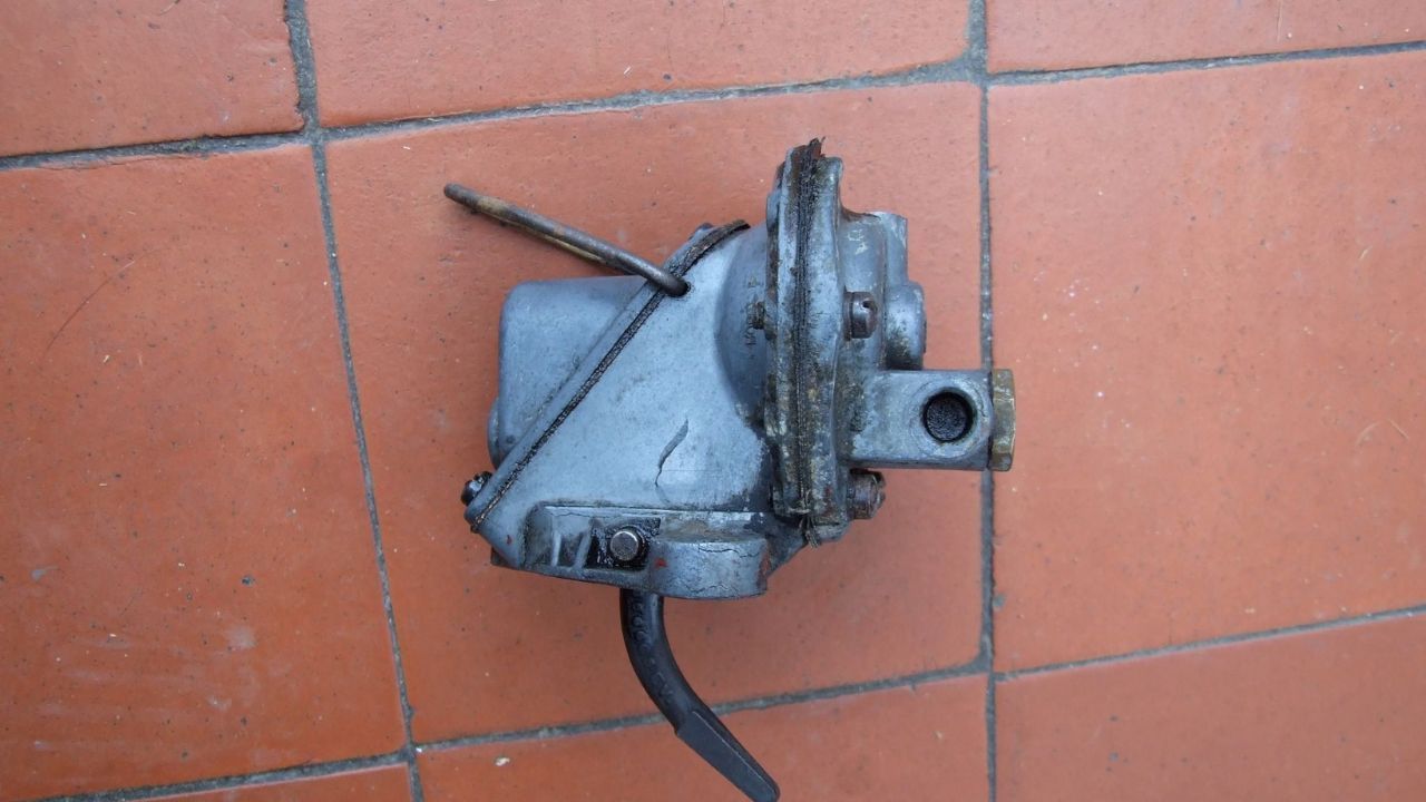 Close-up of a mechanical automotive fuel pump resting on a red tiled surface.