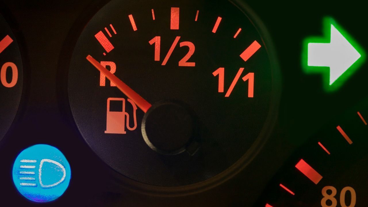 Illuminated car dashboard fuel gauge indicating a nearly empty gas tank near the reserve line.