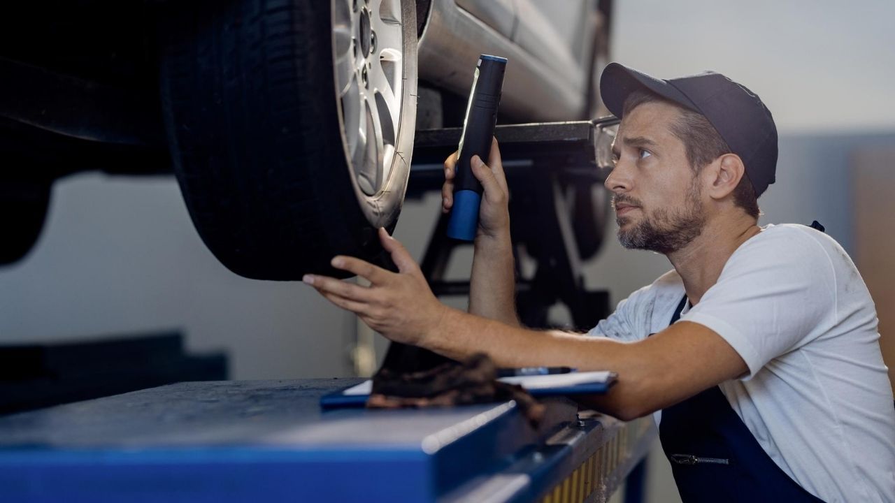 Auto technician inspecting a vehicle tire for alignment and uneven wear.