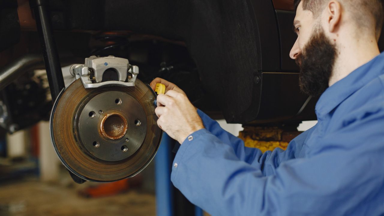 Auto technician measuring brake rotor thickness during a brake system inspection.
