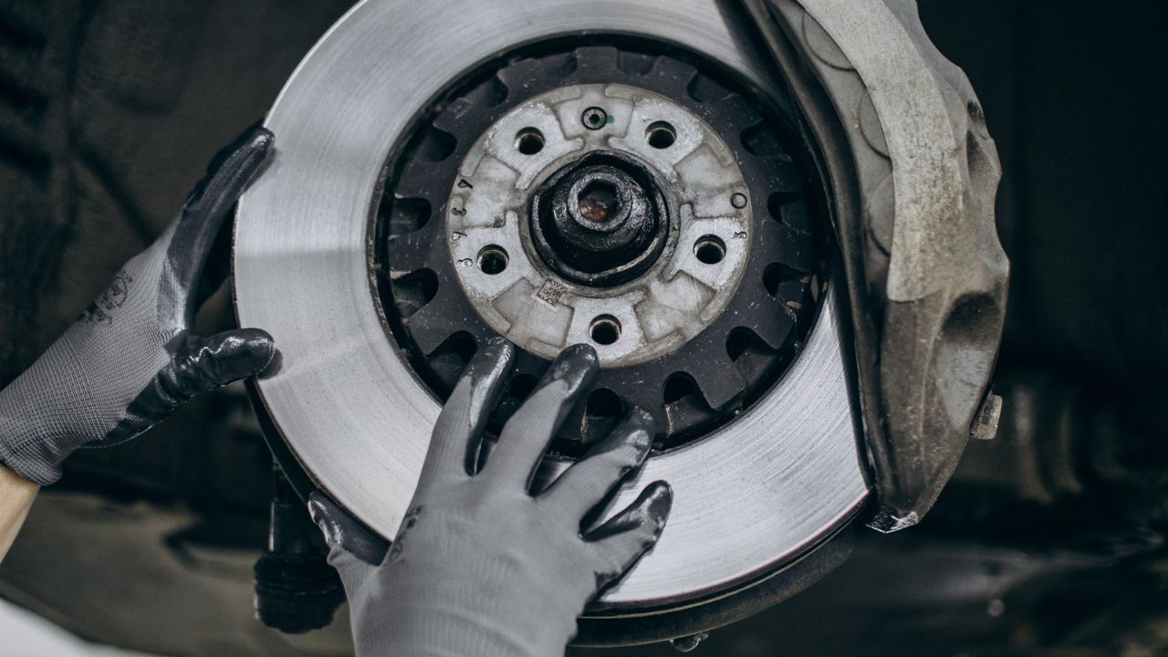 Close-up of a mechanic checking a vehicle brake rotor and brake caliper for wear.