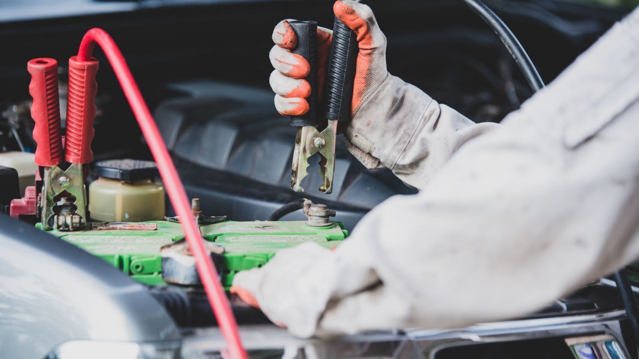 Mechanic connecting jumper cables to a car battery for a safe battery boost.